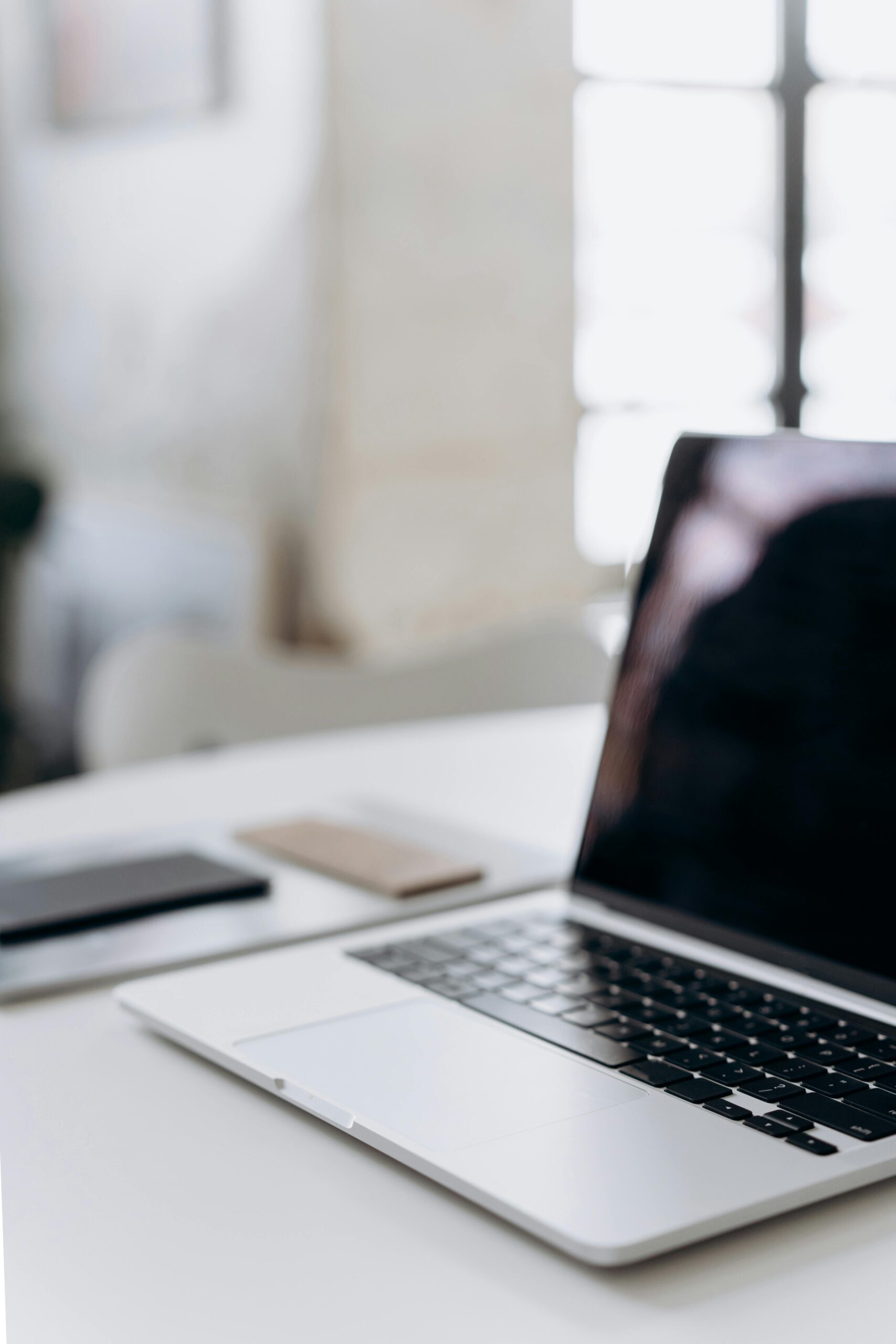Minimalistic workspace featuring a laptop and smartphone on a white table in an office setting.